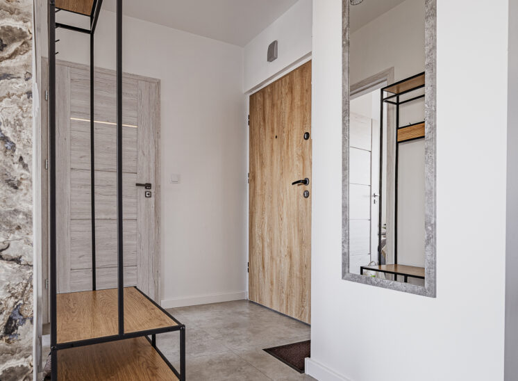 Nowoczesny przedpokój z wejściami do pokoju, salonu i łazienki, urządzony w jasnej, minimalistycznej stylistyce.