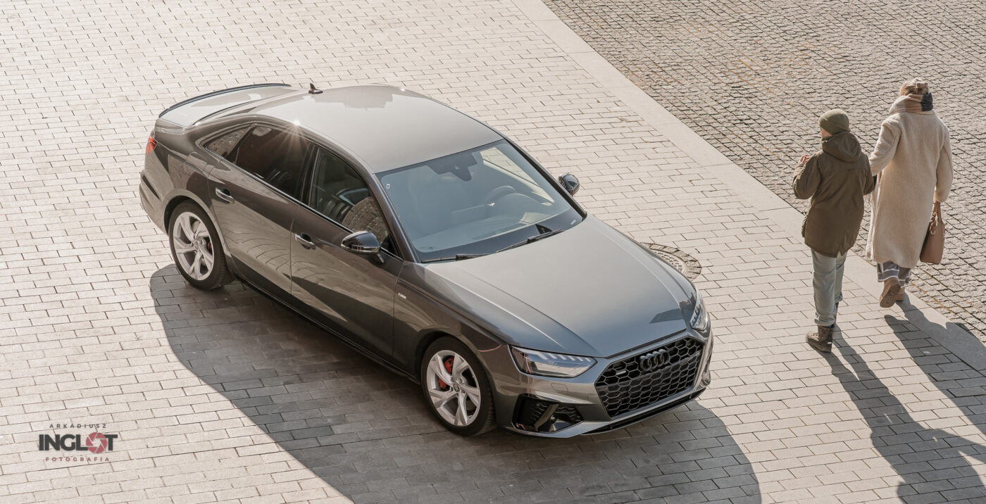 Widok z górnej perpsektywy na grafitowe Audi A4 zaparkowane przed budynkiem NOSPR w Katowicach, z wyraźnie widocznymi eleganckimi liniami nadwozia i nowoczesną architekturą w tle.