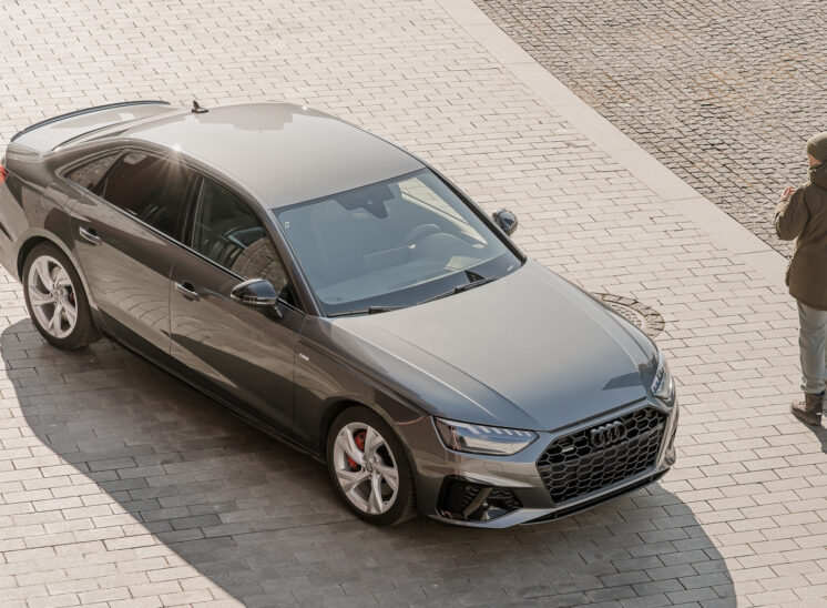 Widok z górnej perpsektywy na grafitowe Audi A4 zaparkowane przed budynkiem NOSPR w Katowicach, z wyraźnie widocznymi eleganckimi liniami nadwozia i nowoczesną architekturą w tle.