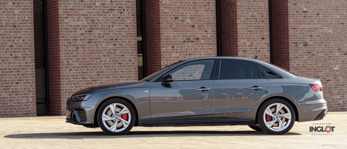 Audi A4 uchwycone od boku, zaparkowane na tle nowoczesnego budynku NOSPR w Katowicach. Profesjonalna fotografia motoryzacyjna podkreślająca dynamiczne linie nadwozia i elegancki design w miejskim otoczeniu.