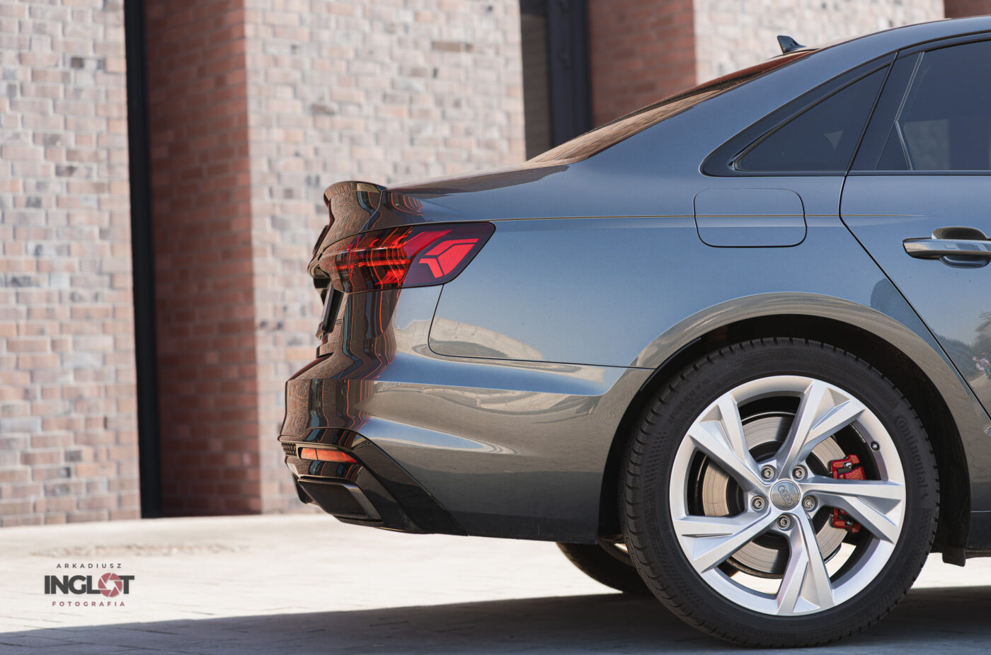 Fragment tylnej części Audi A4 uchwycony z boku, z widocznymi detalami lamp LED i eleganckimi liniami nadwozia, na tle nowoczesnego budynku NOSPR w Katowicach. Profesjonalna fotografia motoryzacyjna w nowoczesnym, miejskim stylu.