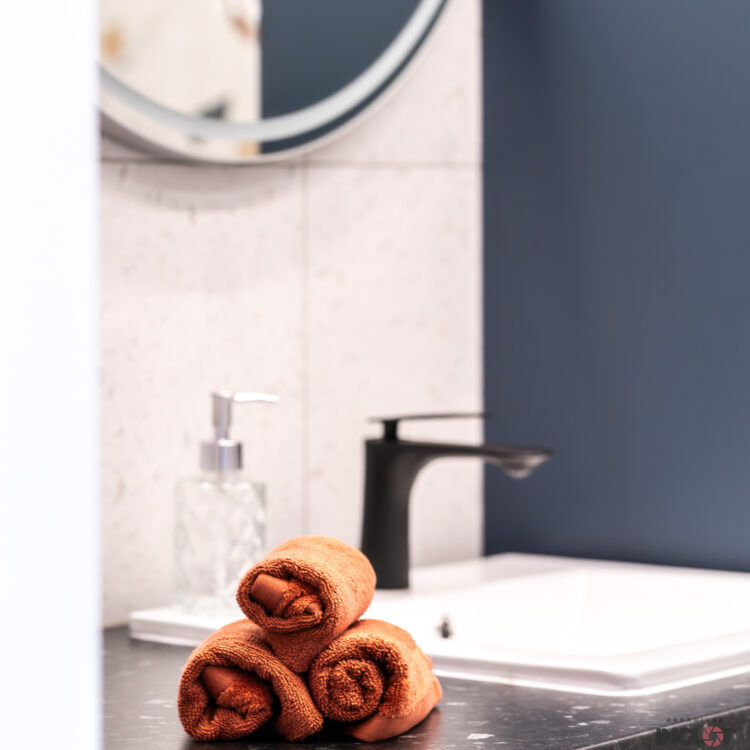 Zwinięte pomarańczowe ręczniki jako dekoracja w stylowej niebiesko-białej łazience – profesjonalna fotografia wnętrz.